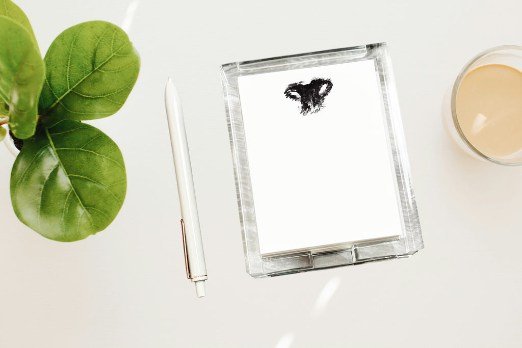 Clear acrylic notepad with nose print on a white surface next to a pen and plant