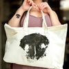 Person holding a tote bag with a black nose print design on a blurred background