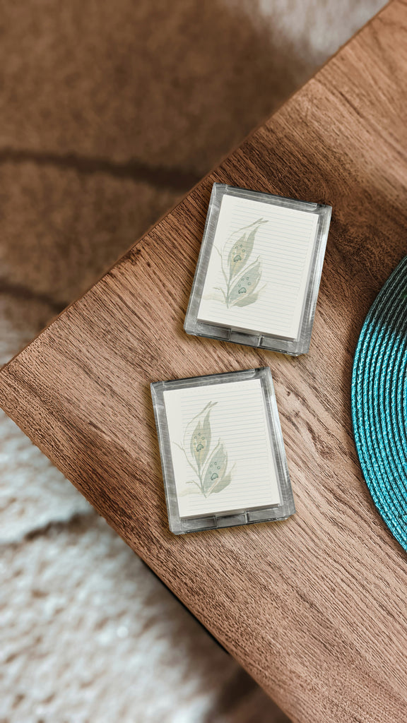 Two small acrylic notepad holders with leaf prints (printed with custom paws) on a wooden surface with a blurred background