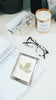 Desk with a candle, glasses, and decorative items on a white surface with a custom acrylic notepad featuring leaf design with paw and snoot print