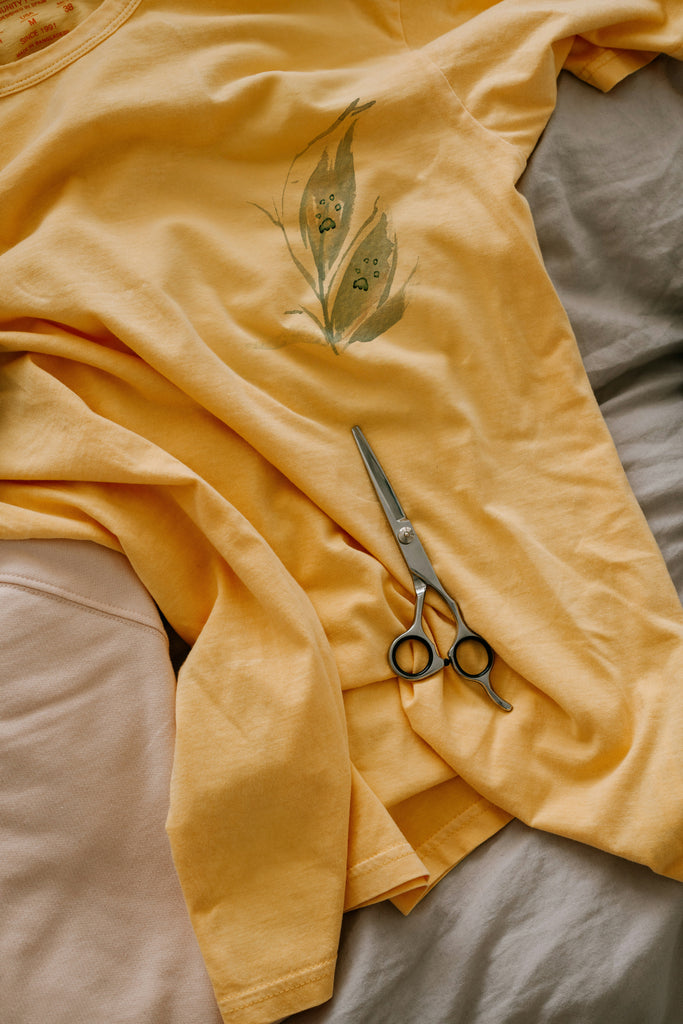 Yellow shirt with a leaf paw design and scissors on a bed