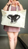 Person holding a tote bag with a black customized dog or cat nose print design against a neutral background