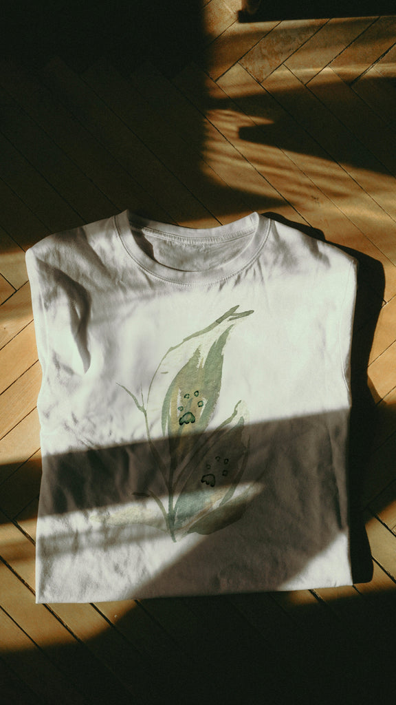 White t-shirt with green paw leaf design on a wooden floor