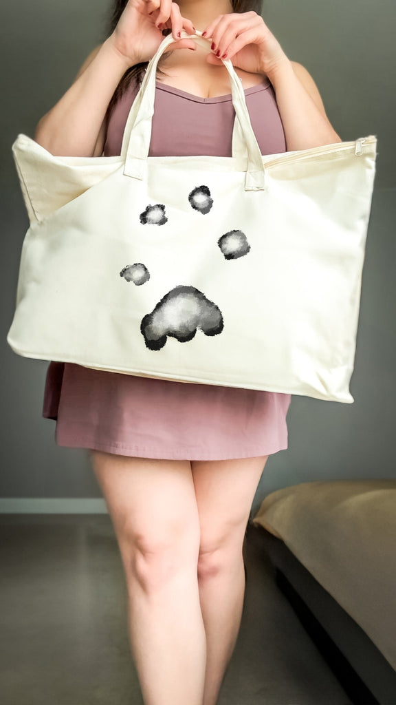 Person holding a tote bag with paw prints impression design on a plain background