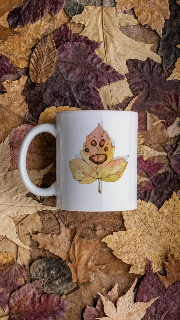 White mug with leaf design on a bed of autumn leaves