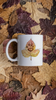 White mug with leaf design on a bed of autumn leaves