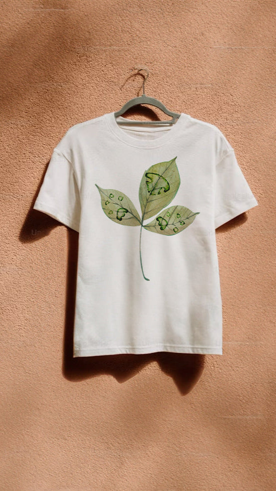 White t-shirt with green leaf with paw prints design on a hanger against a brown wall