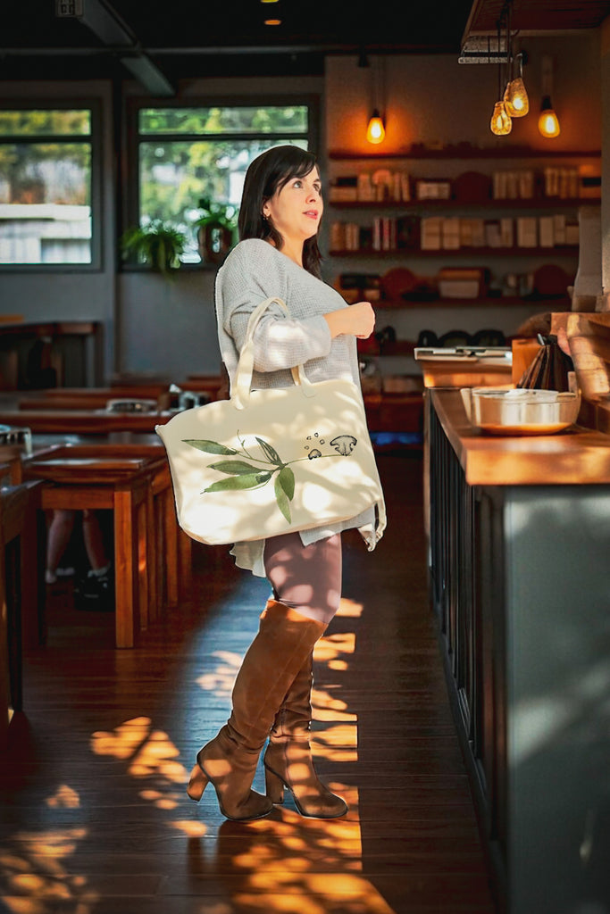 Woman holding a tote bag with green leaves and nose/paw print in a cozy cafe.