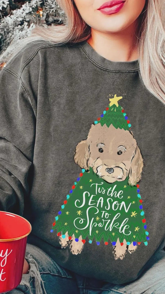 Person wearing a festive sweatshirt with a dog and Christmas tree dog design, holding a red mug.