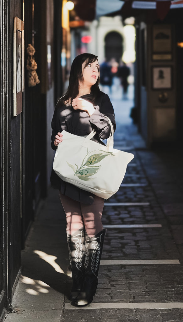 Woman holding a tote bag with paw prints and green leaves in a city alleyway