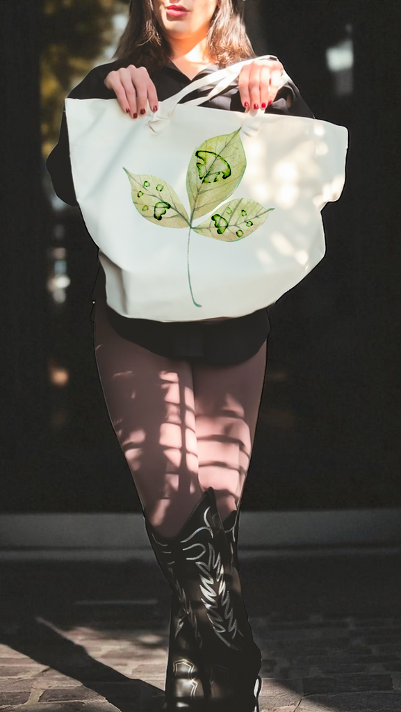 Person holding a tote bag with paw prints on a leaf design against a dark background