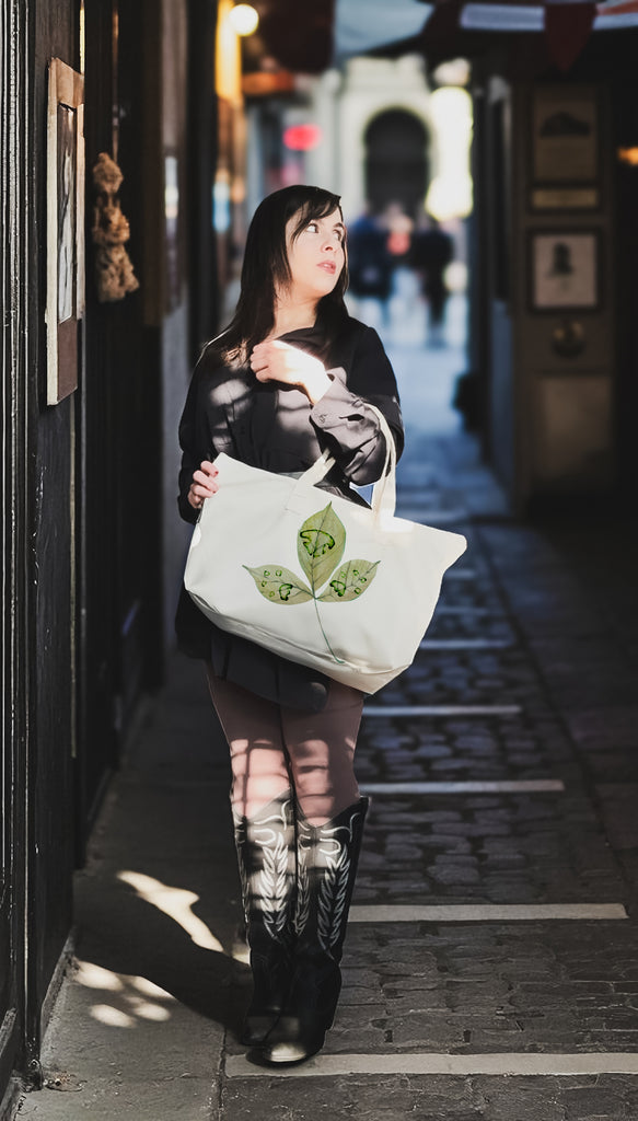 Woman holding a tote bag with a leaf design printed with custom paw prints on a city street.