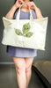 Person holding a tote bag with a leaf design imprinted with a nose print and paw prints against a neutral background