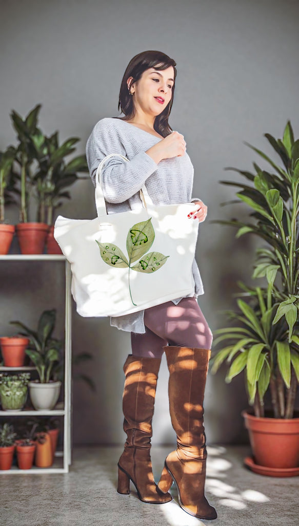 Woman holding a white tote bag with green leaf design imprinted with paw prints and a nose print in a room with plants.