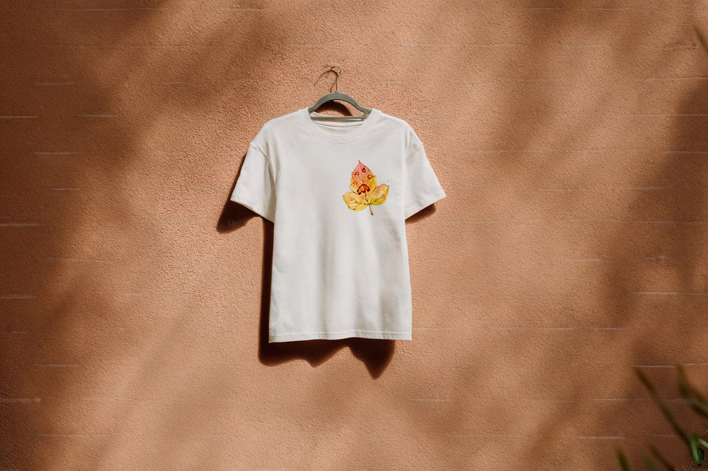 White t-shirt with a colorful paw print on leaf graphic on a hanger against a brown wall