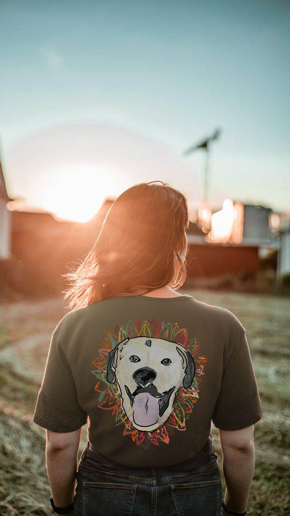 Person wearing a t-shirt with an autumn themed dog graphic, standing in a field with a sunset in the background.