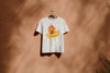 White t-shirt with a colorful leaf/custom paw design on a brown background