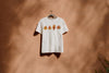 White t-shirt with leaf design imprinted with paw print on a hanger against a brown wall