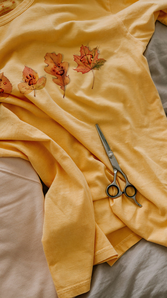 Yellow t-shirt with custom paw prints on autumn leaves design and a pair of scissors on a bed.
