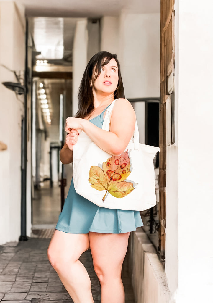 Woman holding a large zipper tote with a custom dog leaf paw design and a blue skirt in an urban setting.