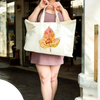 Person holding a white tote bag with a watercolor paw print on leaf design outdoors.