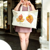 Person holding a tote bag with paw print and autumn leaves design outdoors.