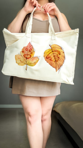 Person holding a tote bag with paw print on leaf design against a neutral background