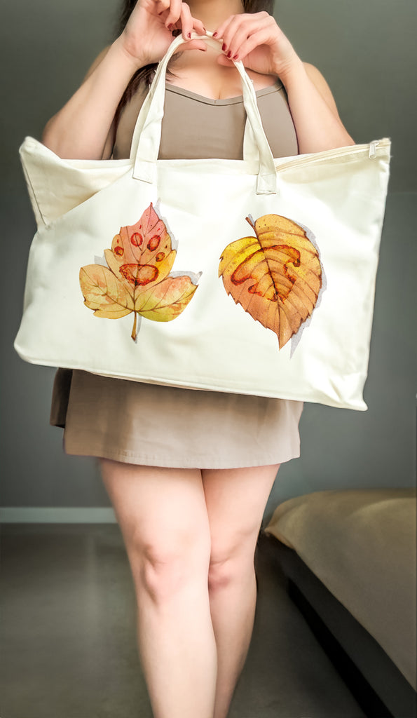 Person holding a tote bag with leaf designs against a neutral background