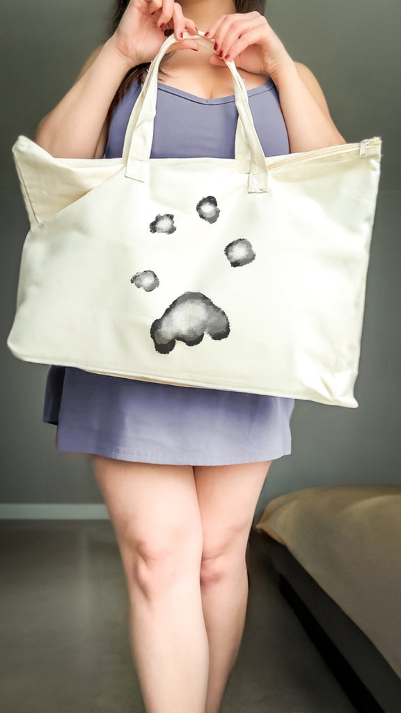 Person holding a tote bag with watercolor paw print on a plain background